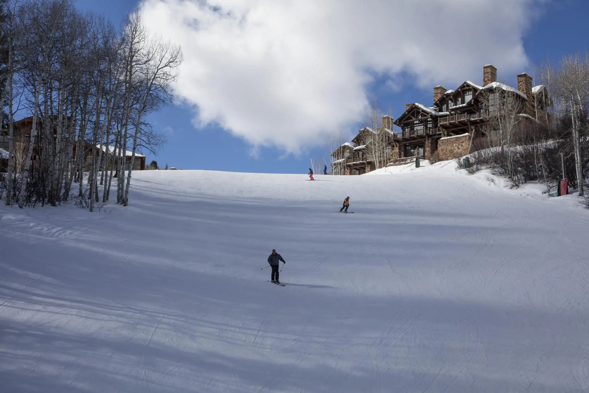 Skiers descending a wide groomed run at Beaver Creek, with timber lodges and aspens at the edge of the slope