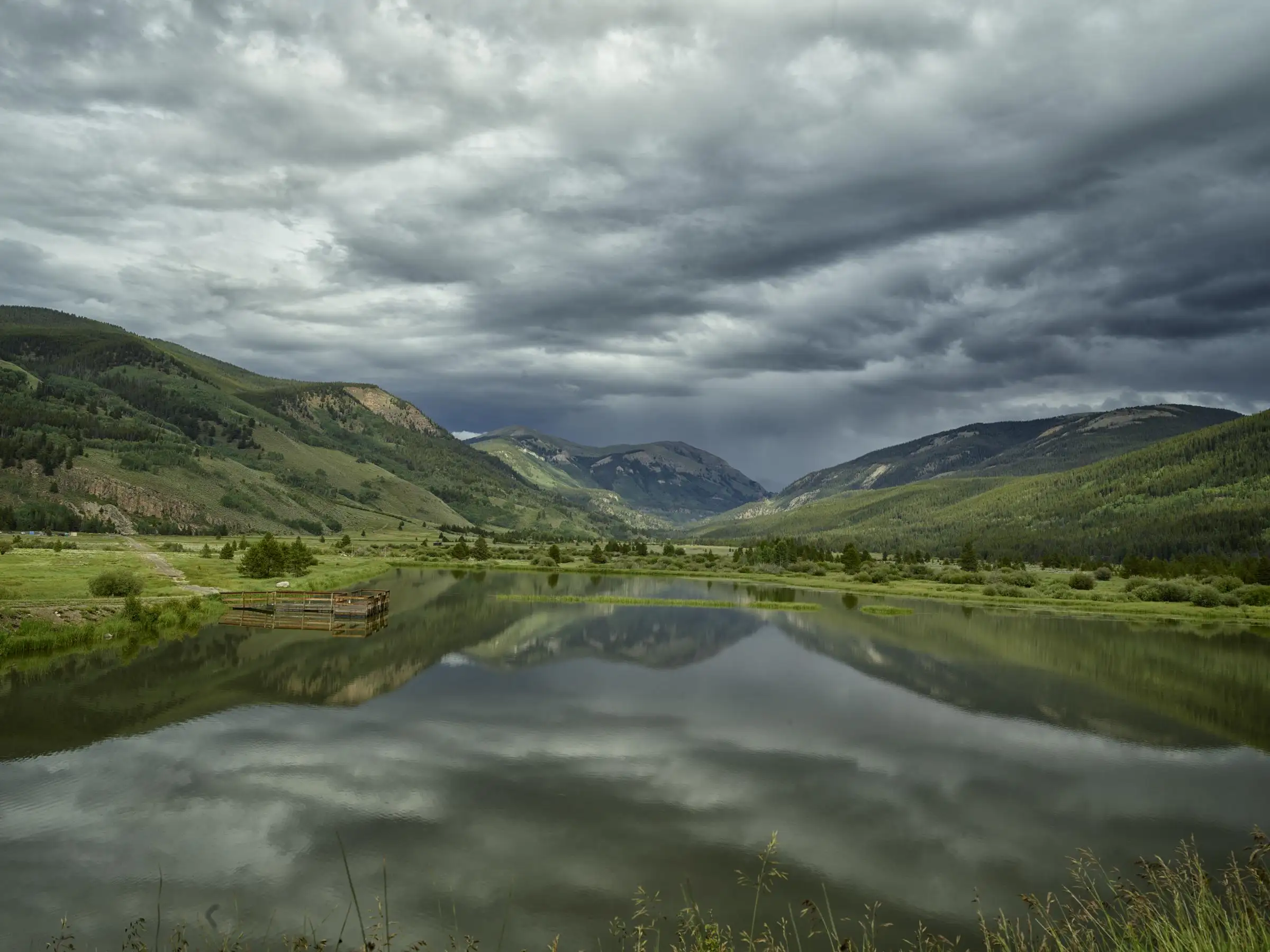 Still water reflecting green mountainsides under storm clouds near the headwaters of the Eagle River